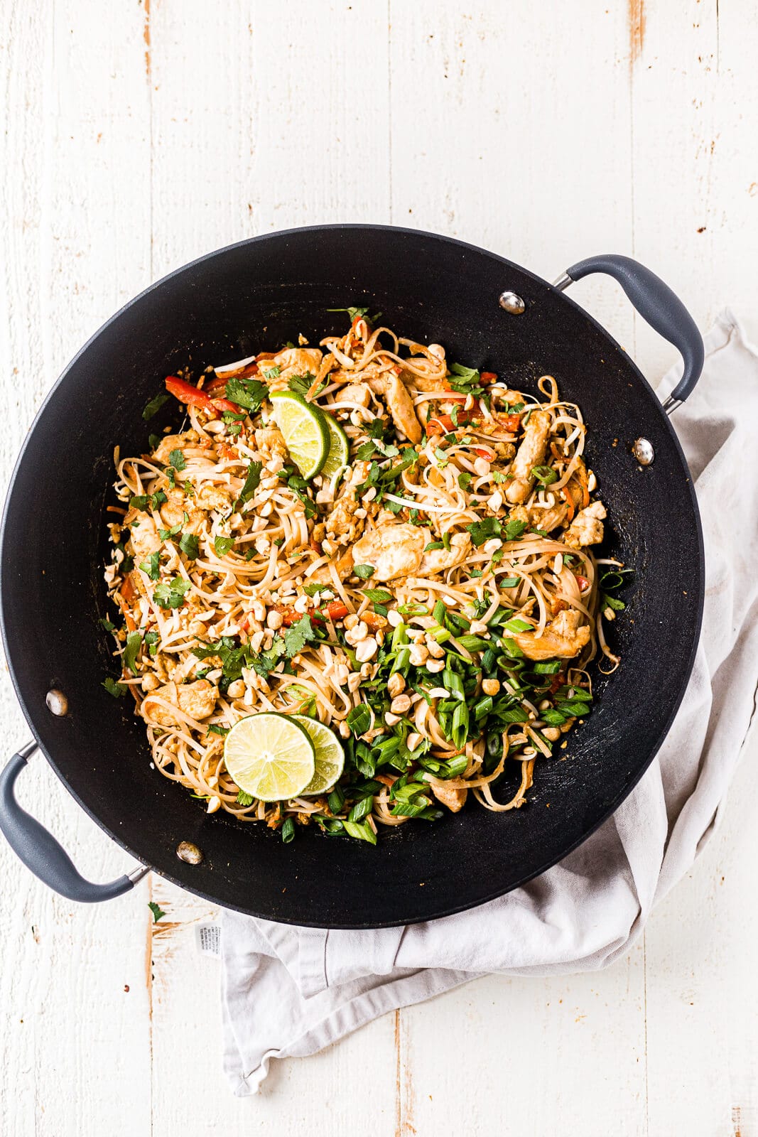 authentic chicken pad thai recipe in a black woke topped with garnishes and lime
