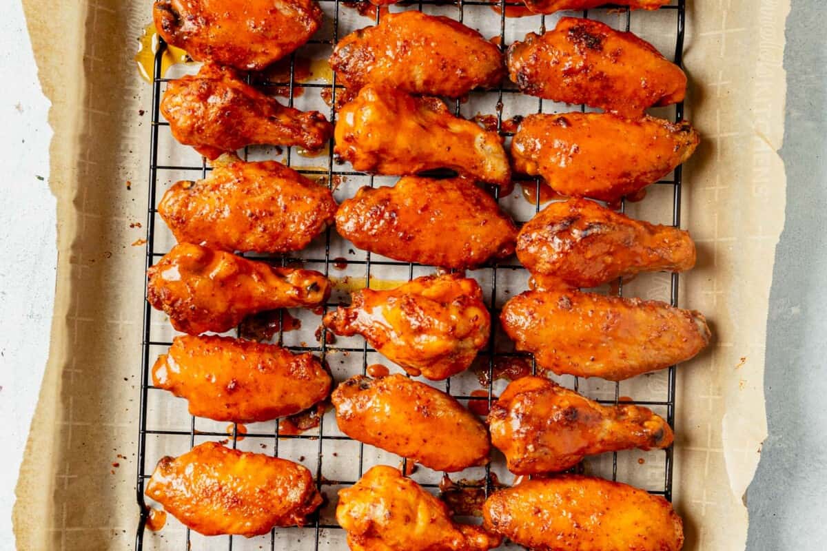 buffalo sauce covering crispy chicken wings on a baking sheet