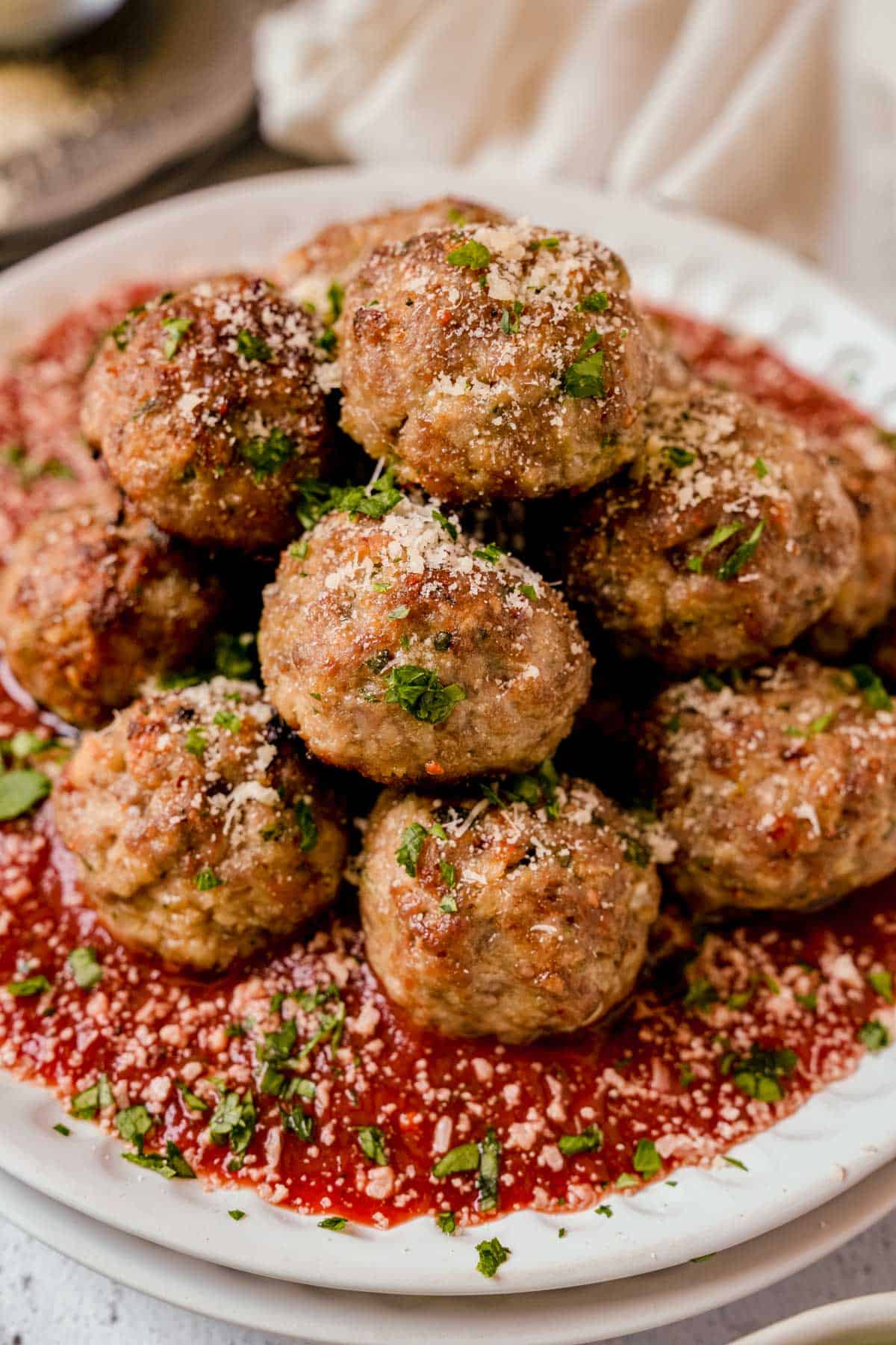 a plate of oven baked meatballs served with marinara sauce on a white plate with parmesan cheese and fresh herbs.