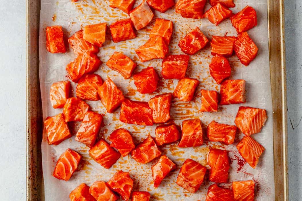 salmon bites seasoned with salt and paprika on a baking sheet