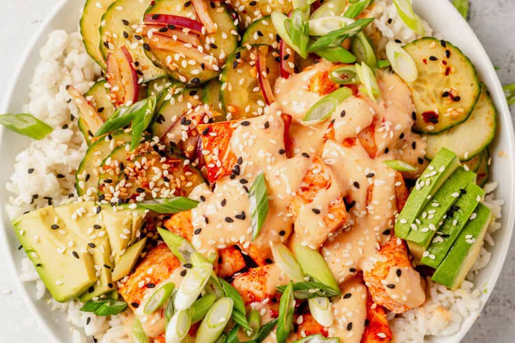 baked salmon covered in bang bang sauce with rice and cucumber salad