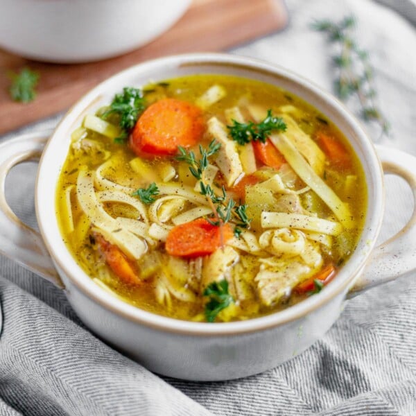 instant pot chicken noodle soup in a white bowl with fresh thyme and parsley