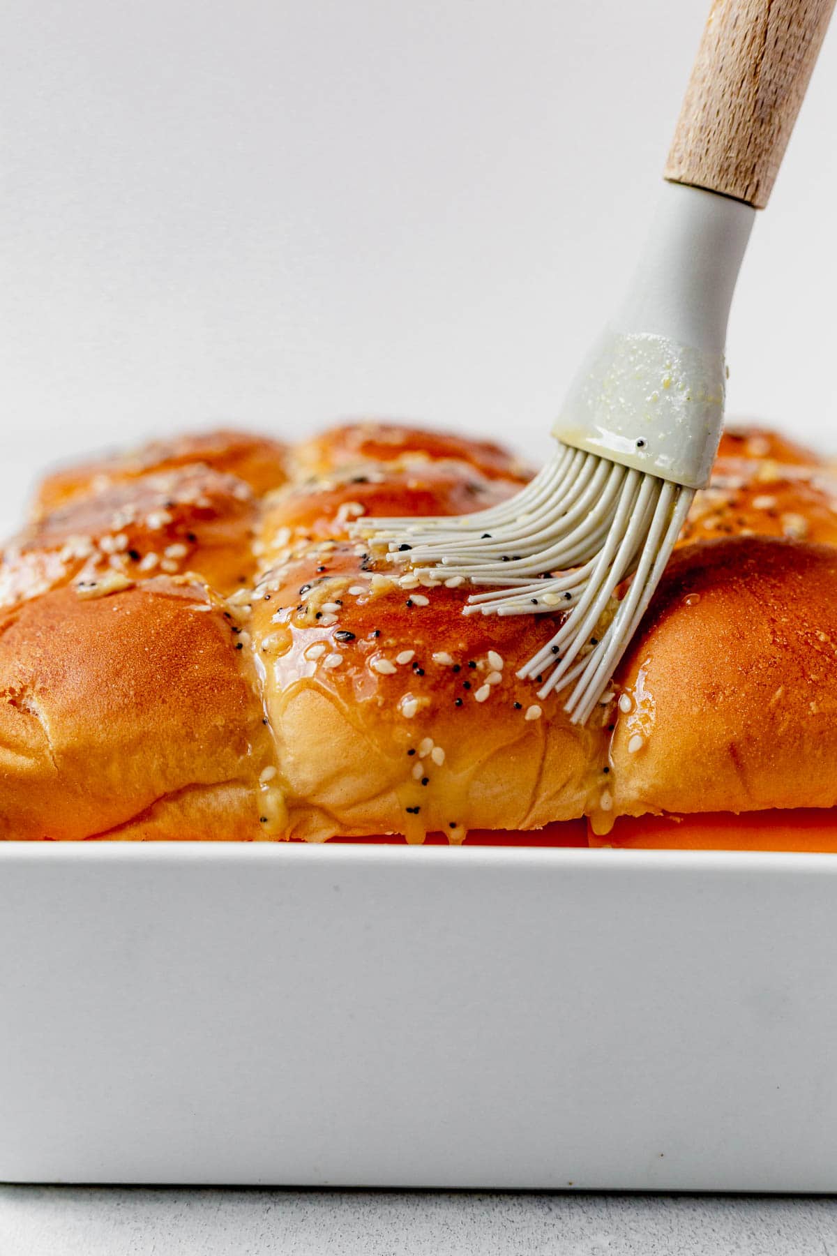 pastry brush brushing butter and maple syrup glaze on top of everything bagel breakfast sliders