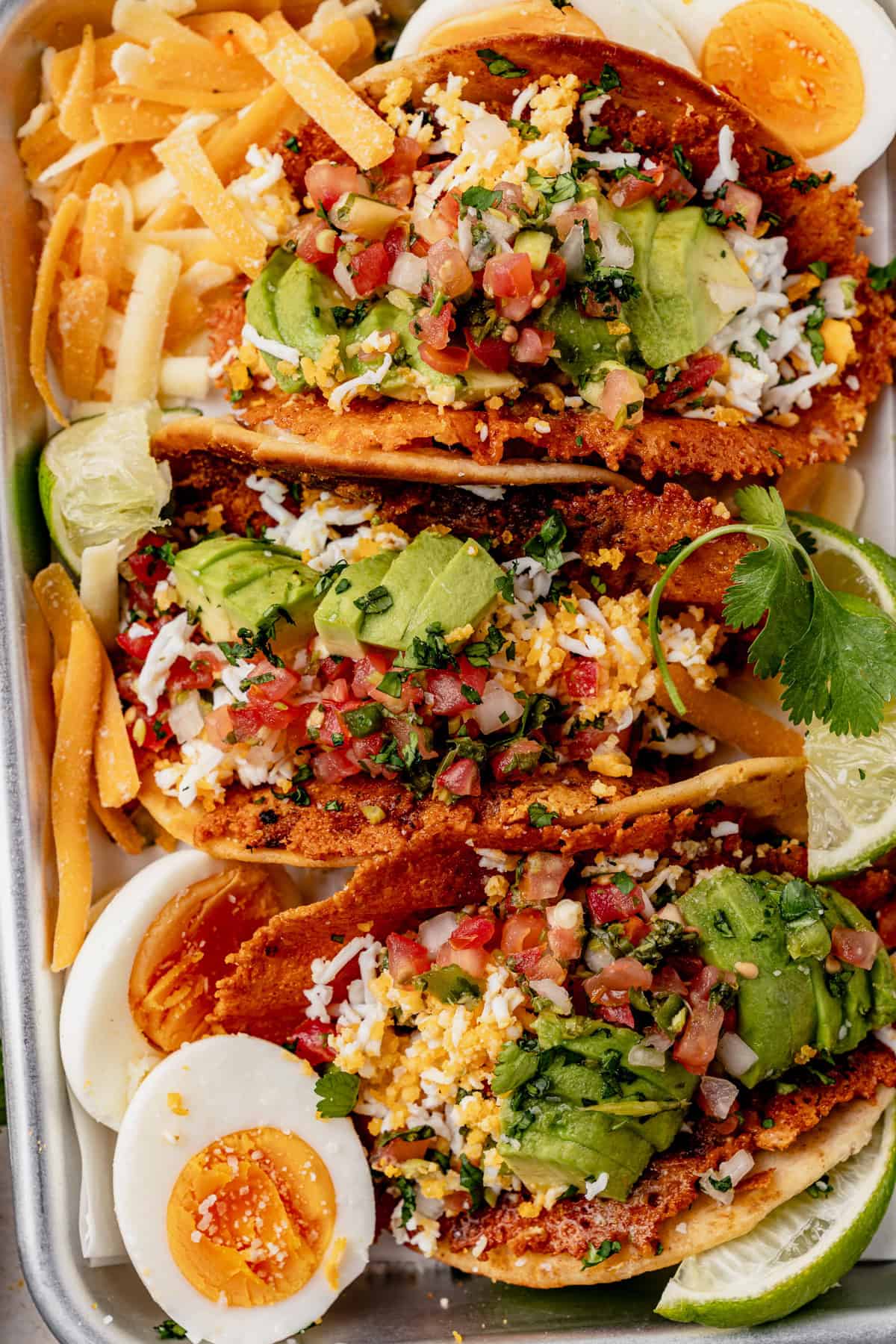three breakfast smash tacos on a tray topped with cilantro, avocado, and pico de gallo.