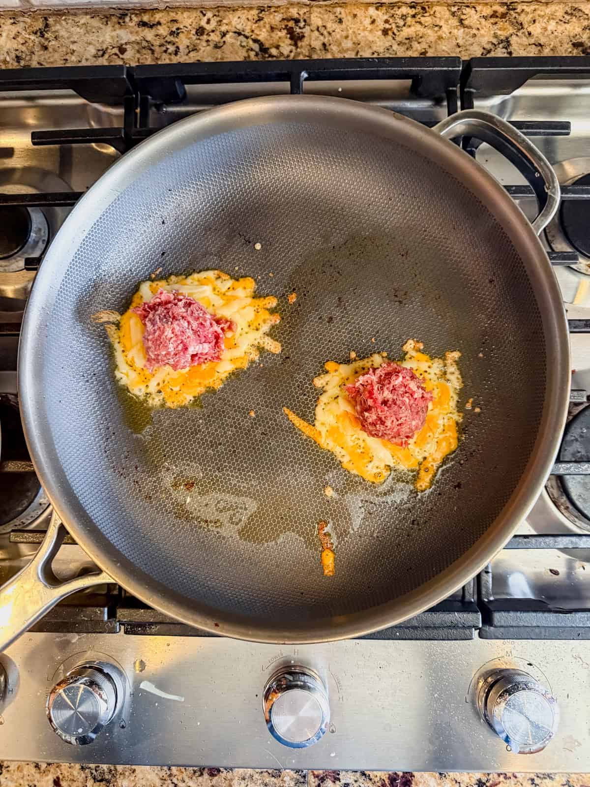 two circles of melted cheese in a skillet with breakfast on top.