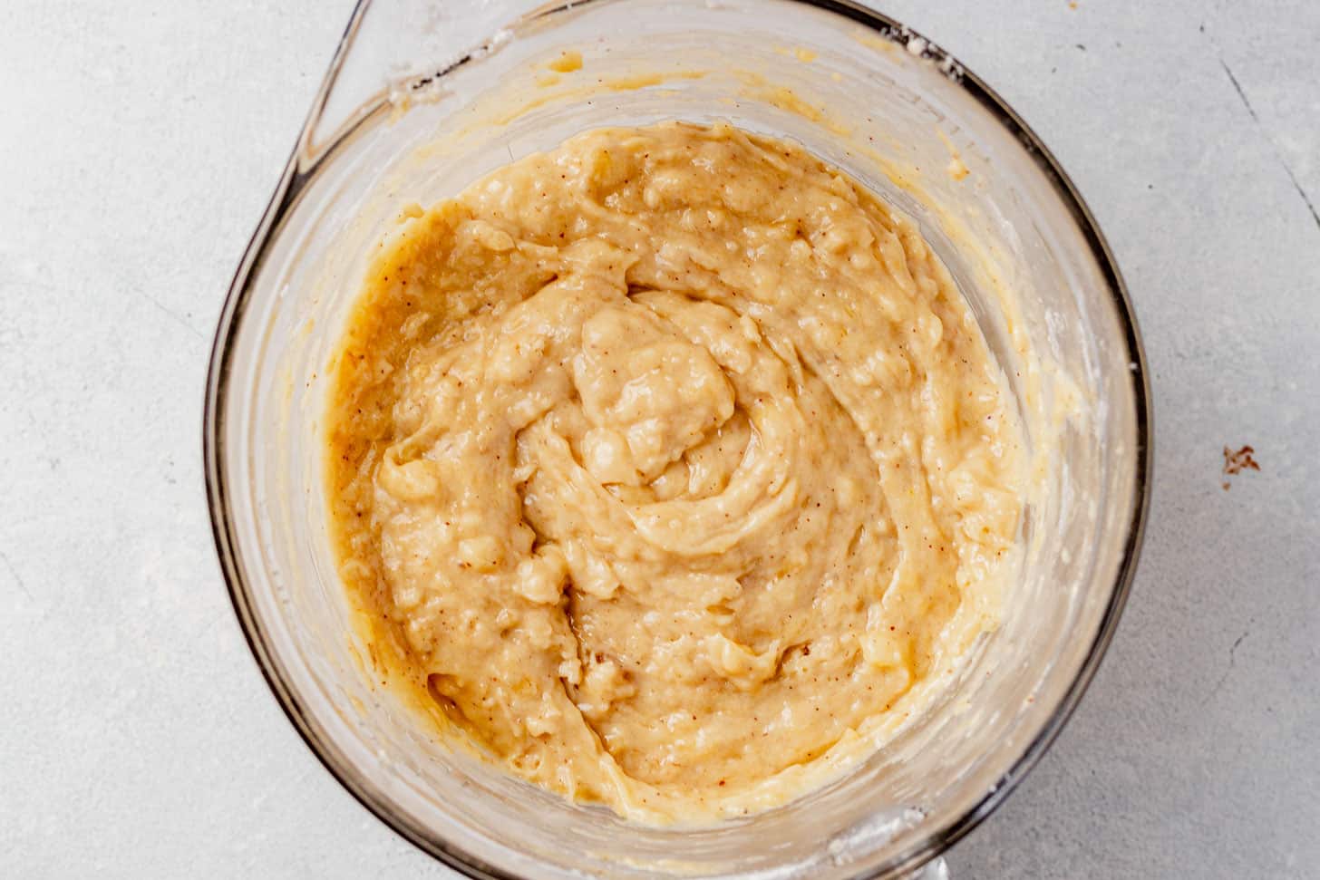 Glass bowl filled with thick, creamy banana bread batter speckled with browned butter and mashed bananas, ready to be poured into a loaf pan.