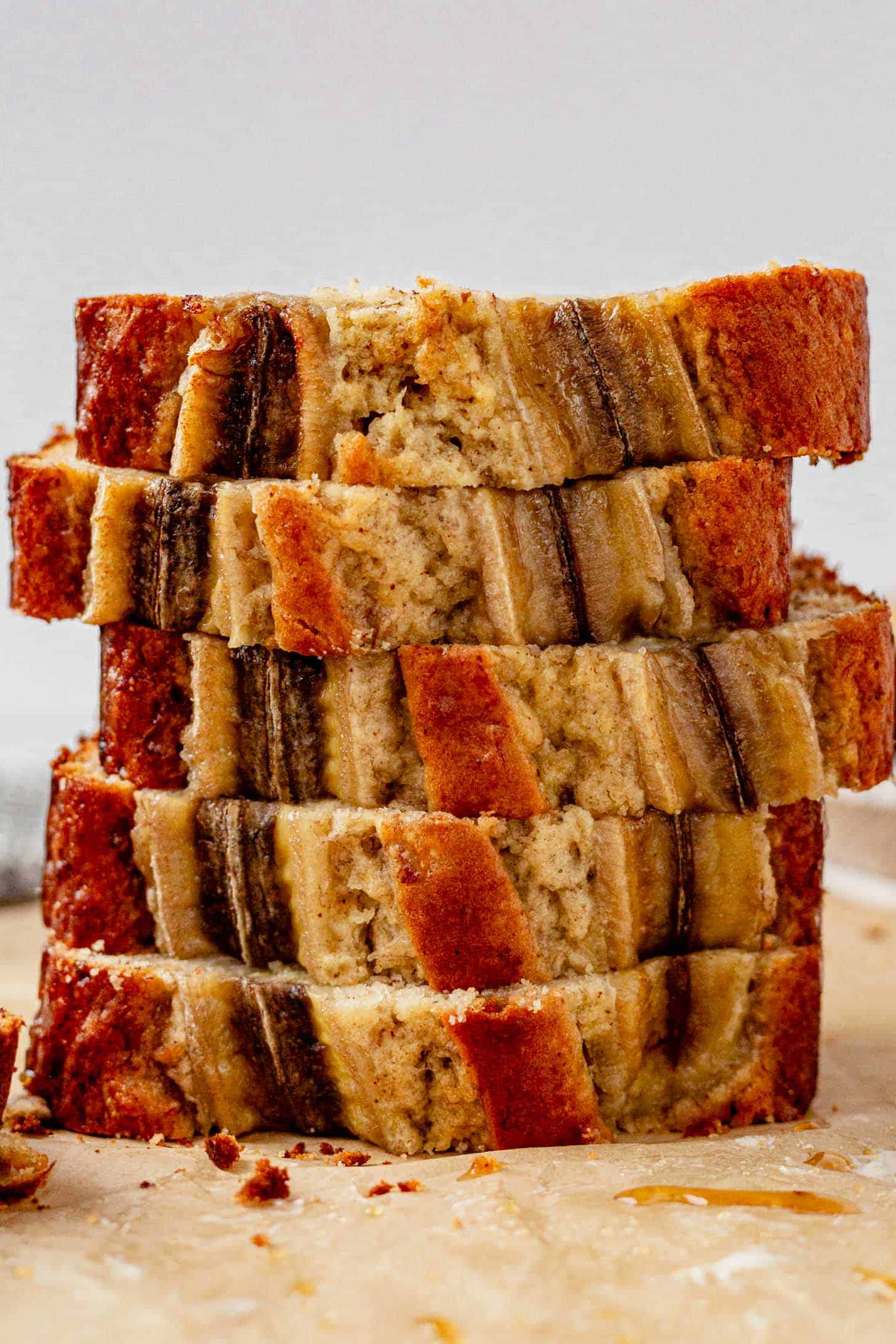 Stack of thick, brown butter banana bread slices topped with caramelized banana strips, showcasing a golden-brown crust and fluffy interior on a parchment-lined surface.