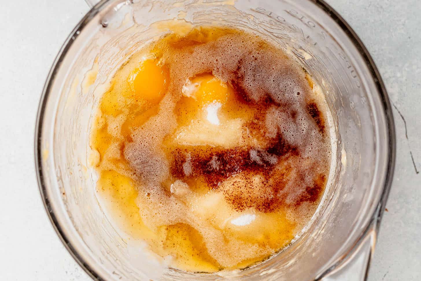 Top-down view of wet ingredients in a glass bowl, including eggs, browned butter, sugar, and sour cream, ready to be mixed.