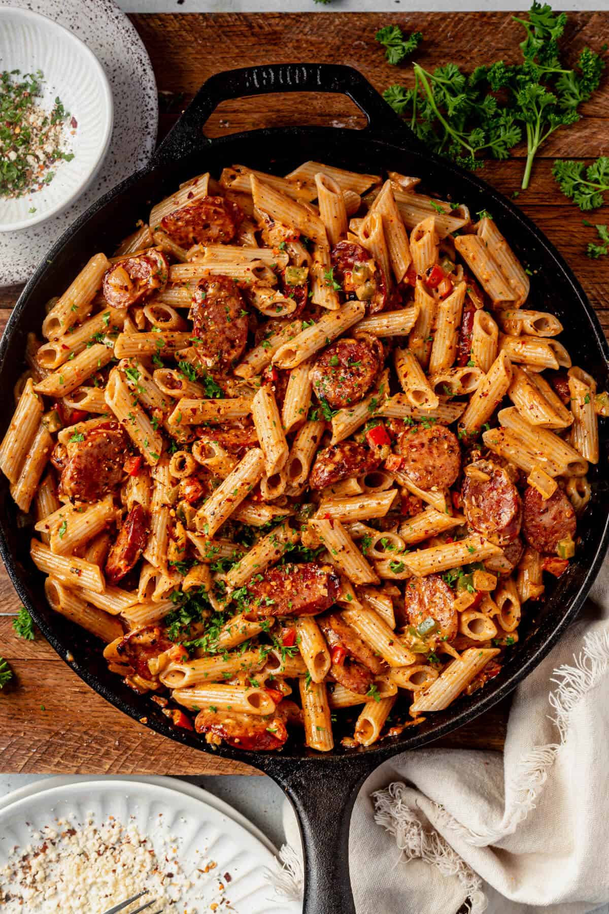 a cast iron skillet full of creamy cajun sausage pasta garnished with parsley.