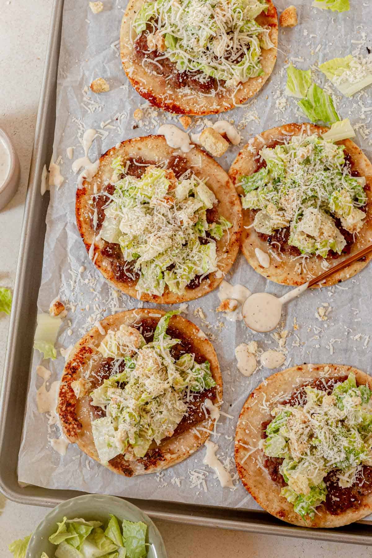 ground chicken smashed tacos topped with caesar salad, dressing, and parmesan cheese.