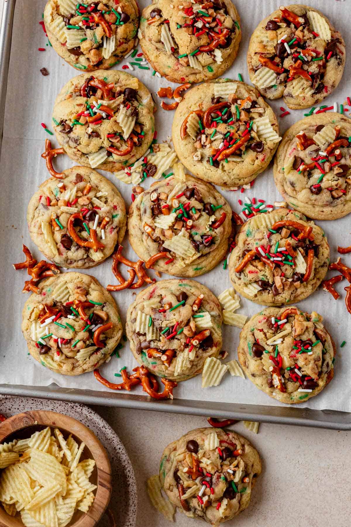 a cookie tray of christmas kitchen sink cookies with a bowl of chips next to it.