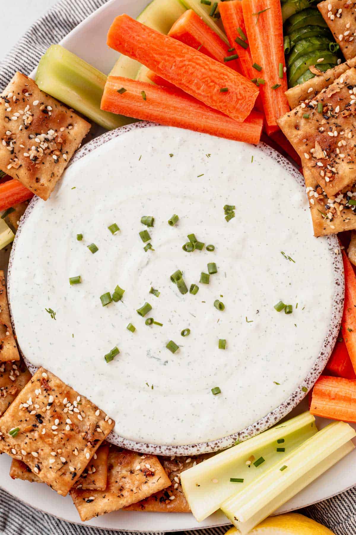 a bowl of cottage cheese dip surround by carrots and seasoned crackers