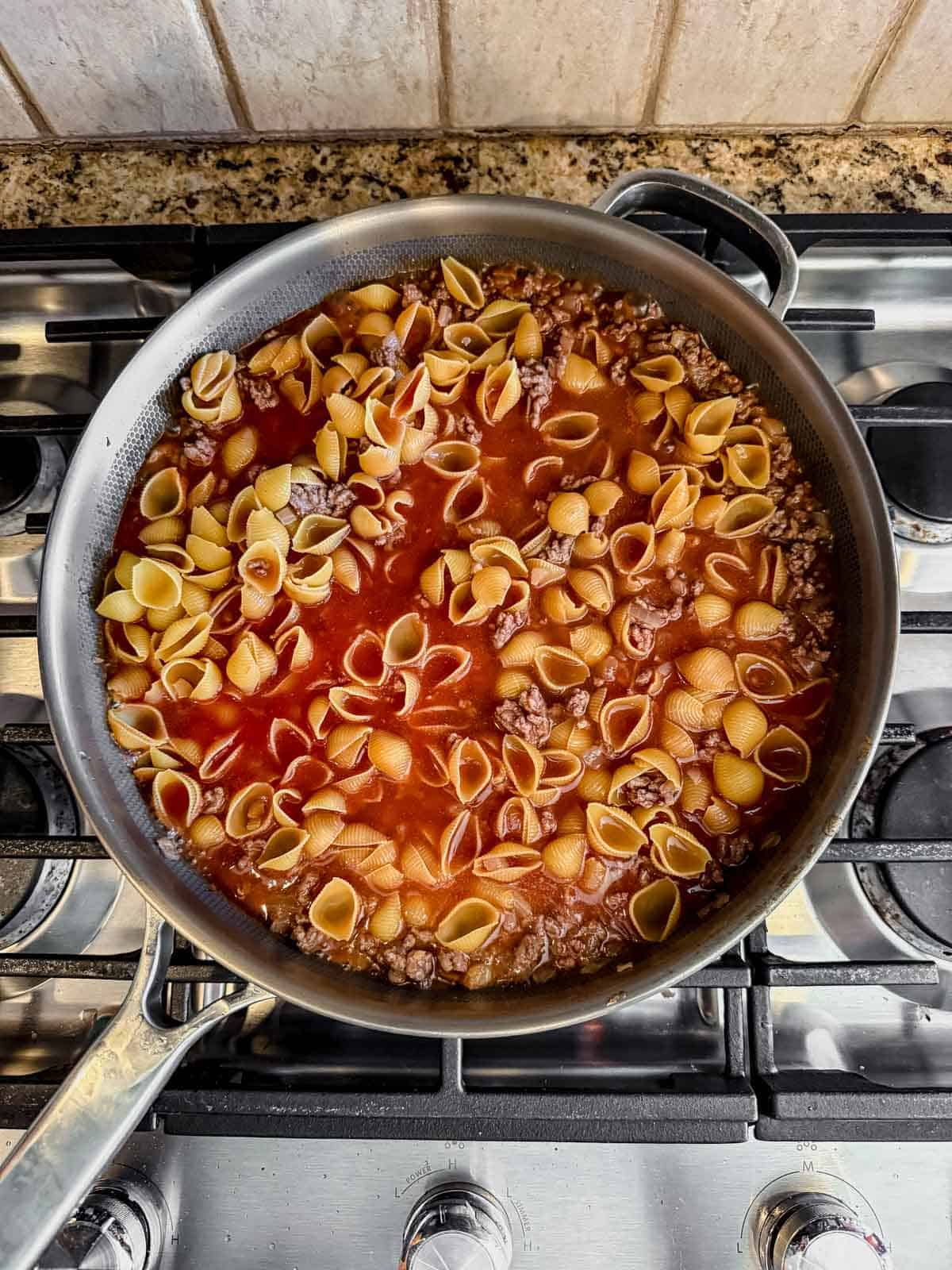 cooked ground beef and onion mixed with uncooked pasta shells in a skillet before simmering.