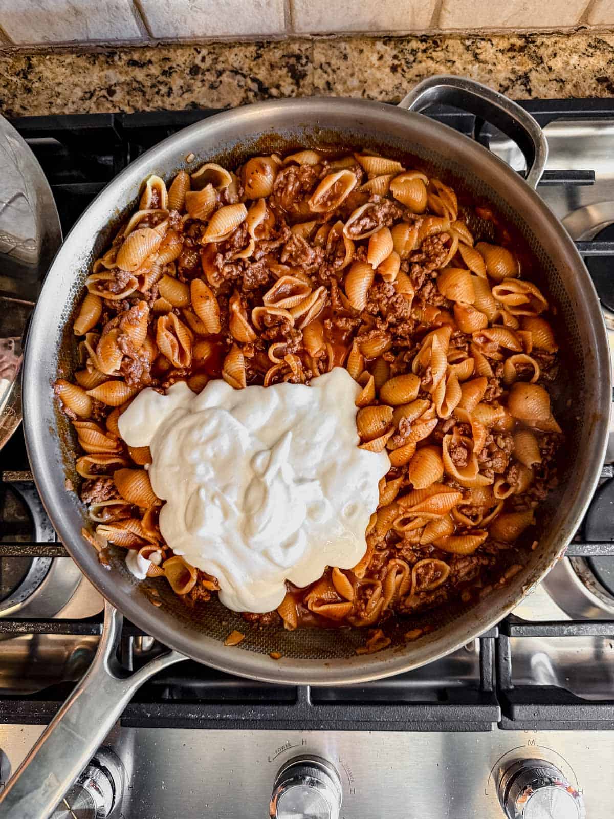 A mixture of heavy cream and cottage cheese on top of cooked beef and shells in a skillet.