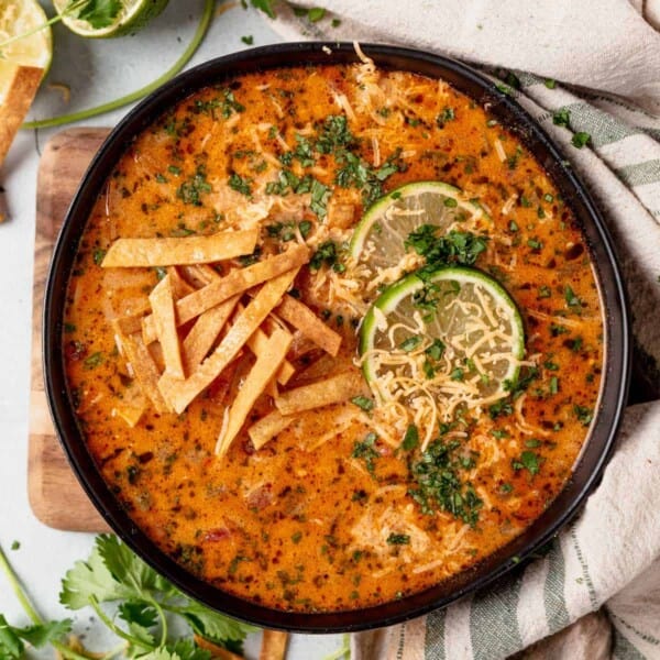 a bowl of creamy chicken tortilla soup topped with limes, tortilla strips and cheese