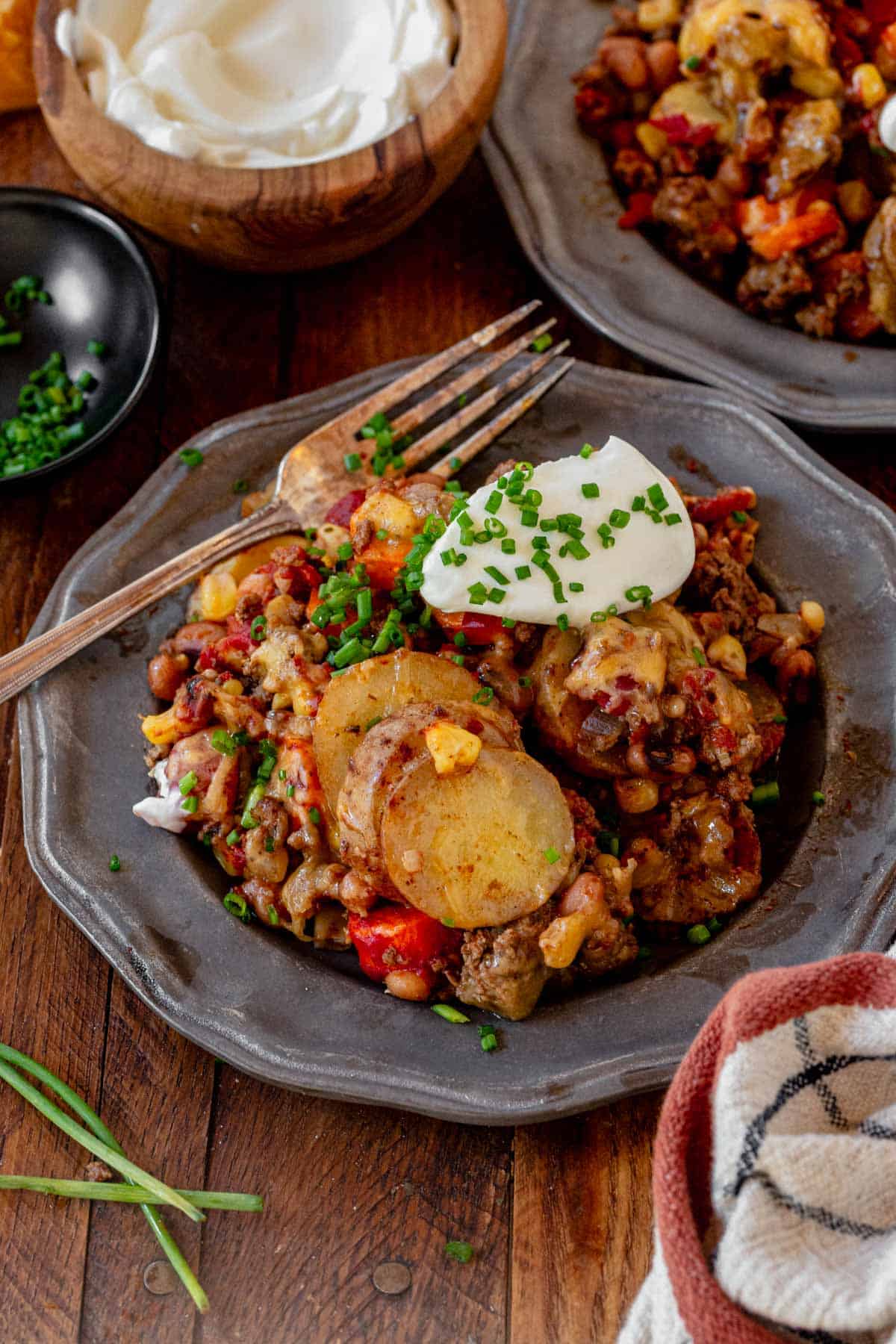 cowboy casserole on a plate with sour cream, chives, and a fork.