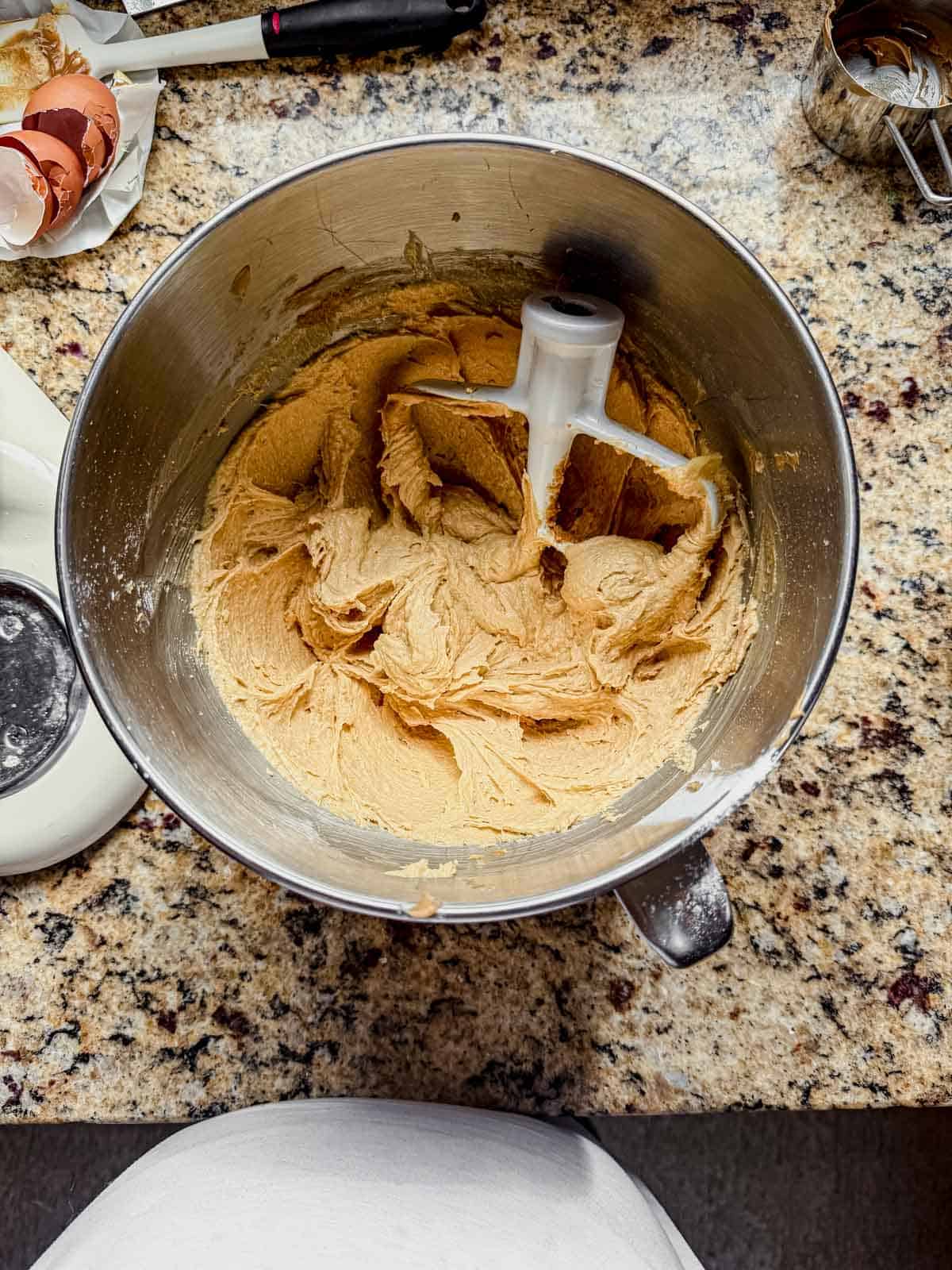 large bowl of a stand mixer and paddle attachment on top of batter of creamed butter, brown sugar, granulated sugar, and peanut butter for fluffernutter cookies.