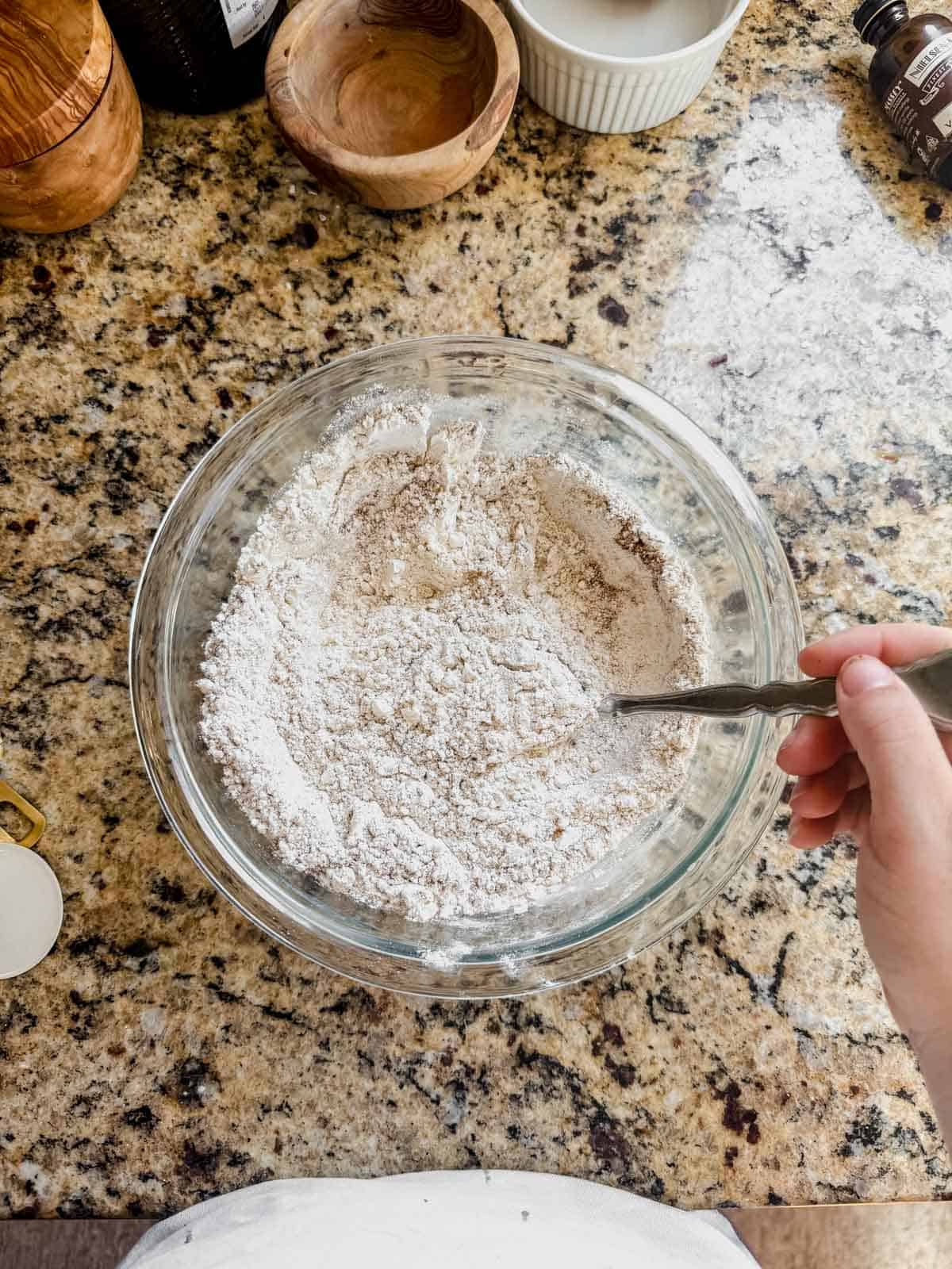 whisking dry ingredients for gingerbread latte cookies in a glass bowl.