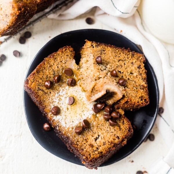 two pieces of almond flour banana bread on a black dessert plate topped with melted butter and chocolate chips