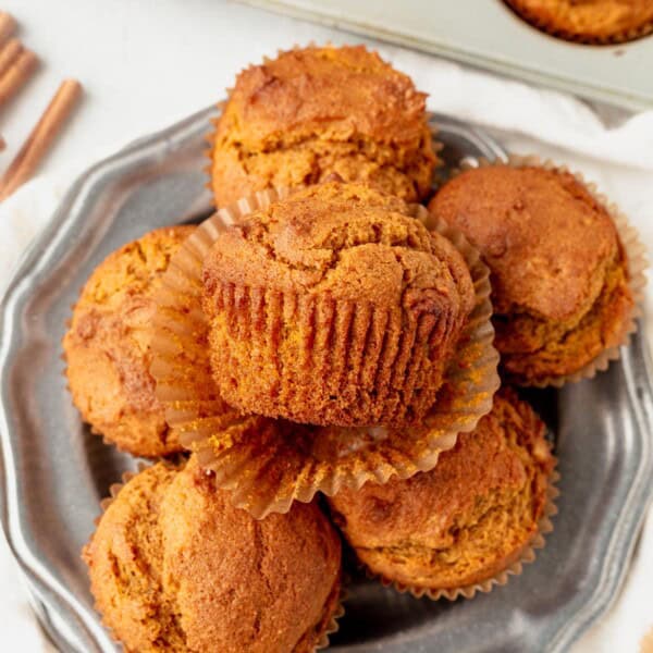 gluten free pumpkin muffins stacked on a plate. top muffin has the muffin wrapper unwrapped