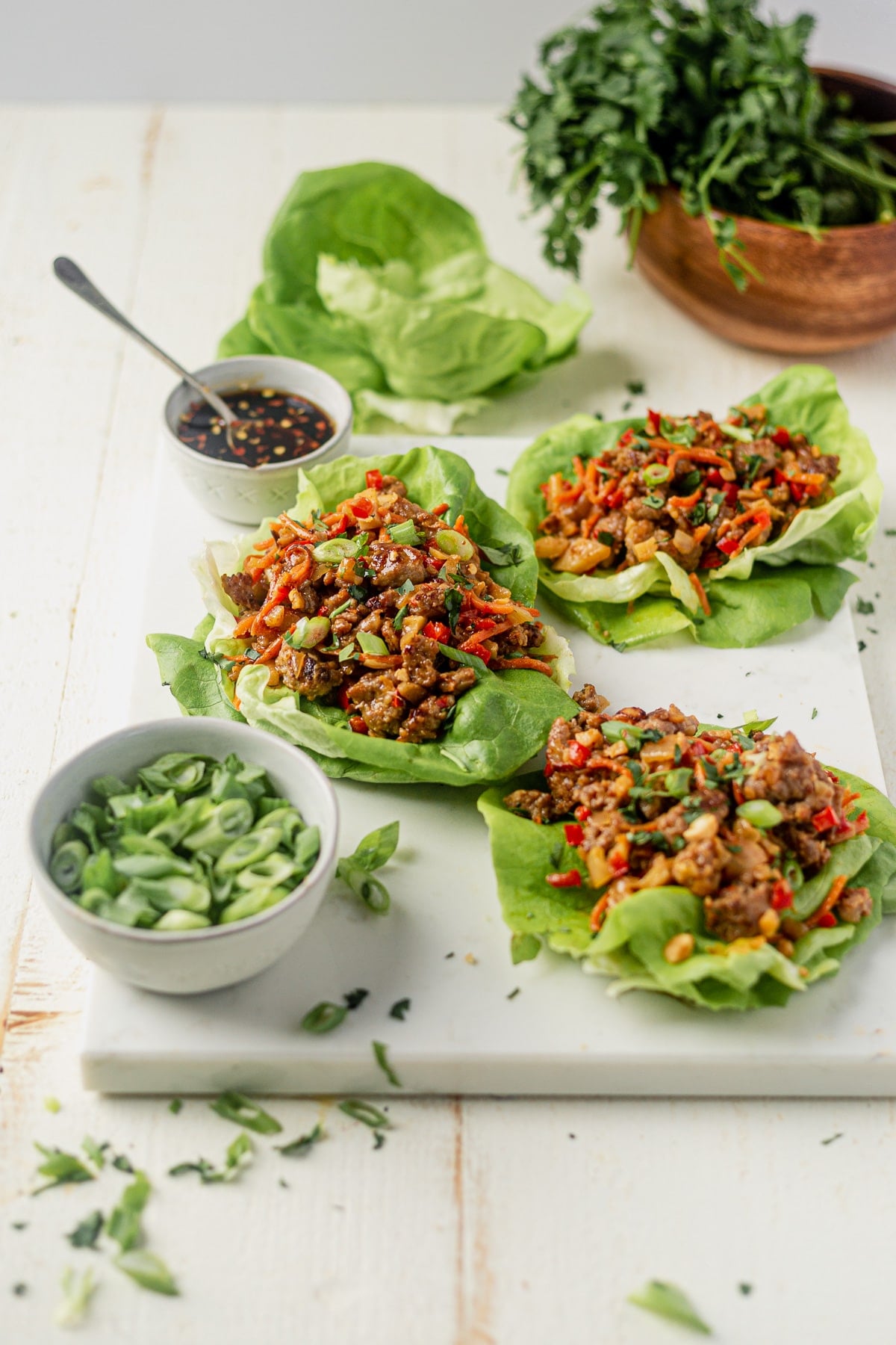 three ground pork lettuce wraps on a white serving tray with sweet and spicy sauce and scallions on the side