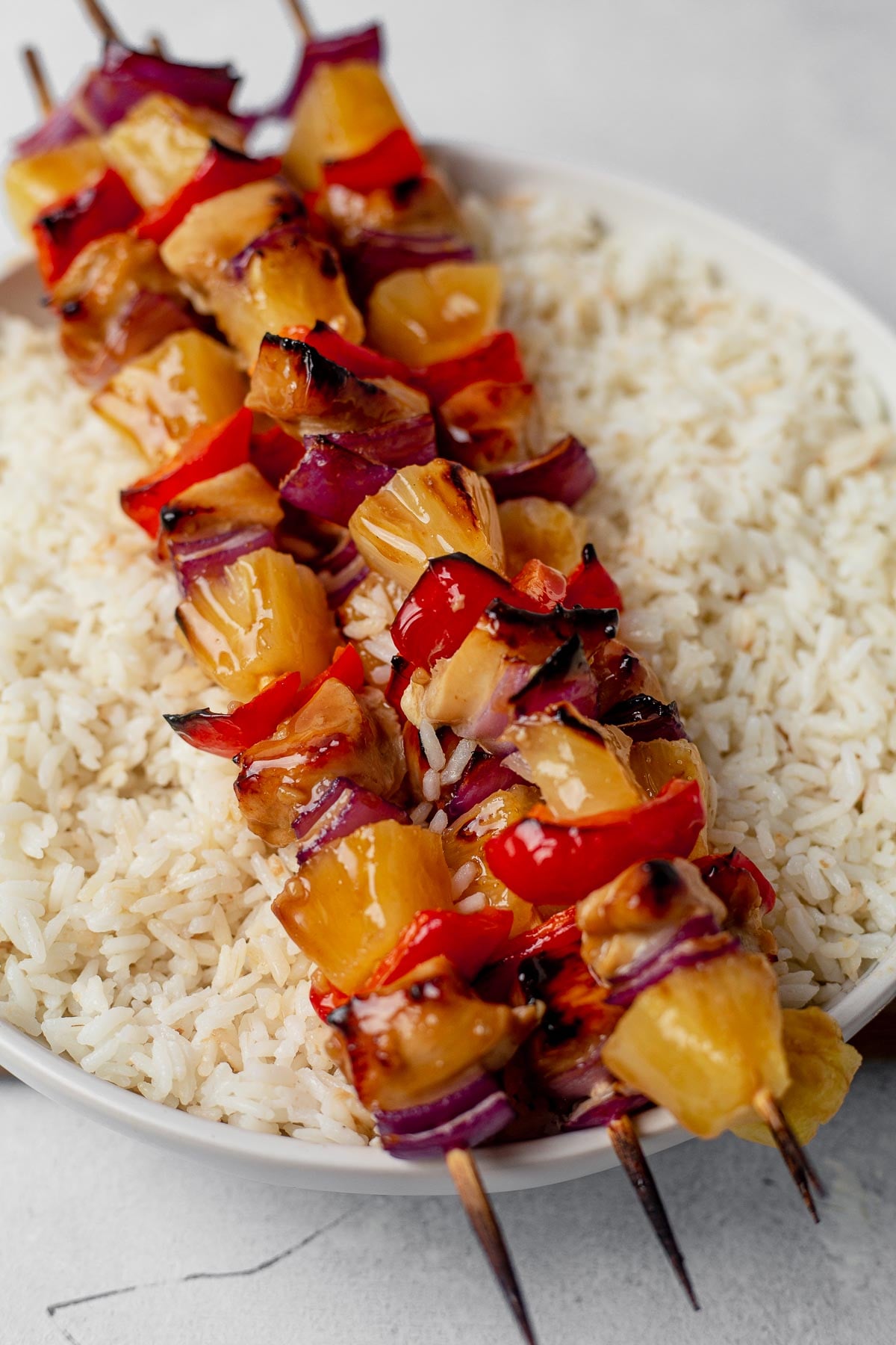 three oven baked pineapple chicken kabobs sitting on top of a bowl of coconut rice.