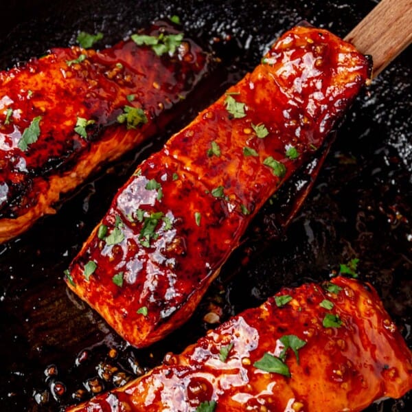 a spatula picking up a honey glazed salmon filet from a skillet