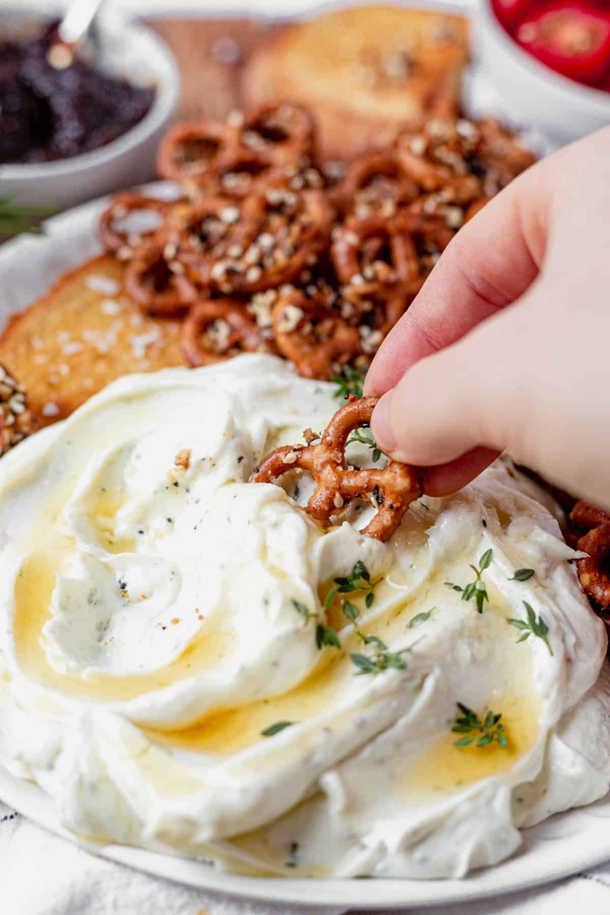 dipping a pretzel into a bowl of creamy whipped goat cheese topped with honey and thyme.