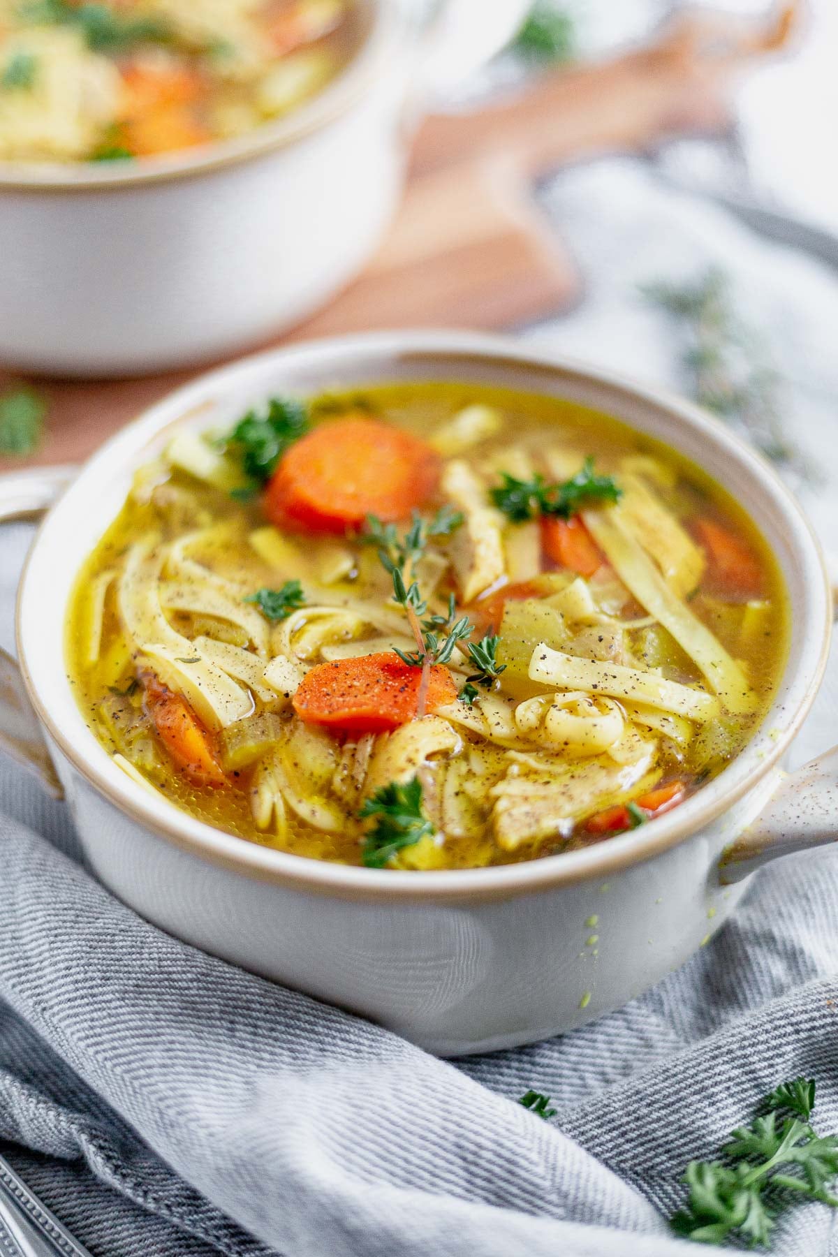 two bowls of instant pot chicken noodle soup on a grey napkin topped with parsley