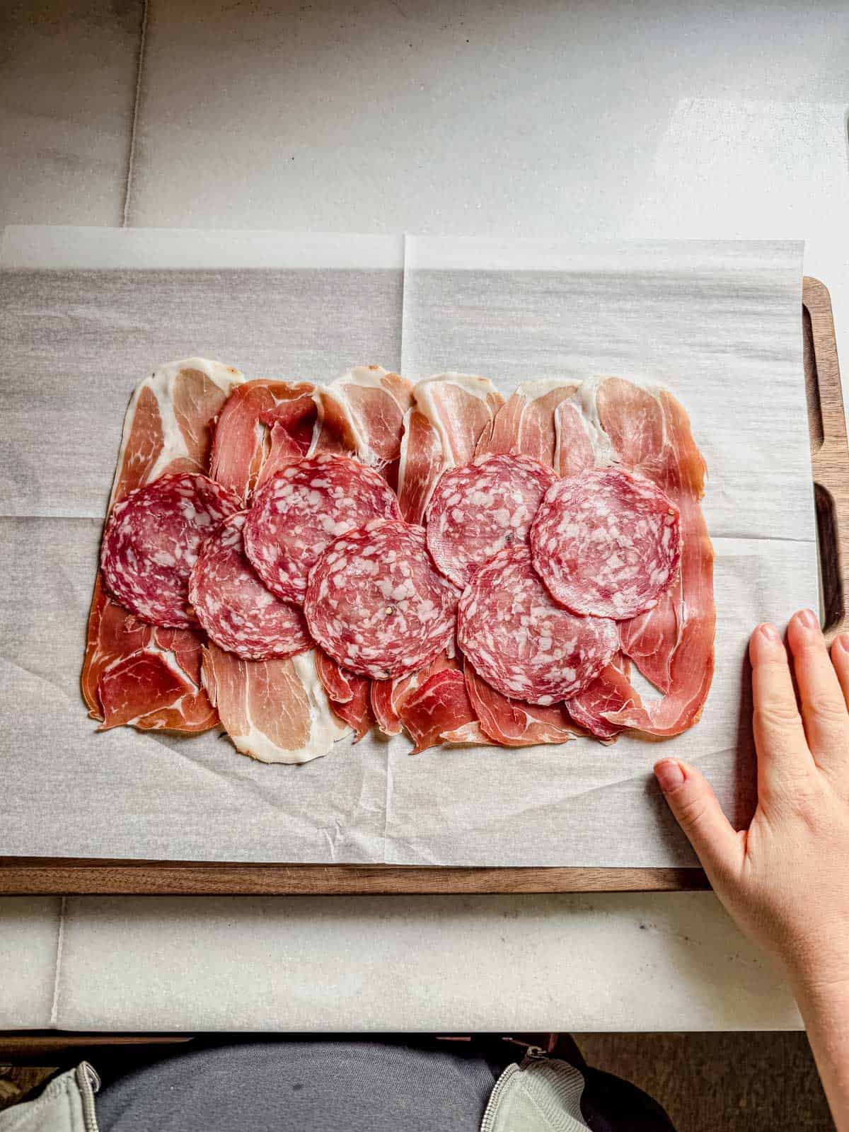 proscuitto and salami layered on a piece of parchment paper.