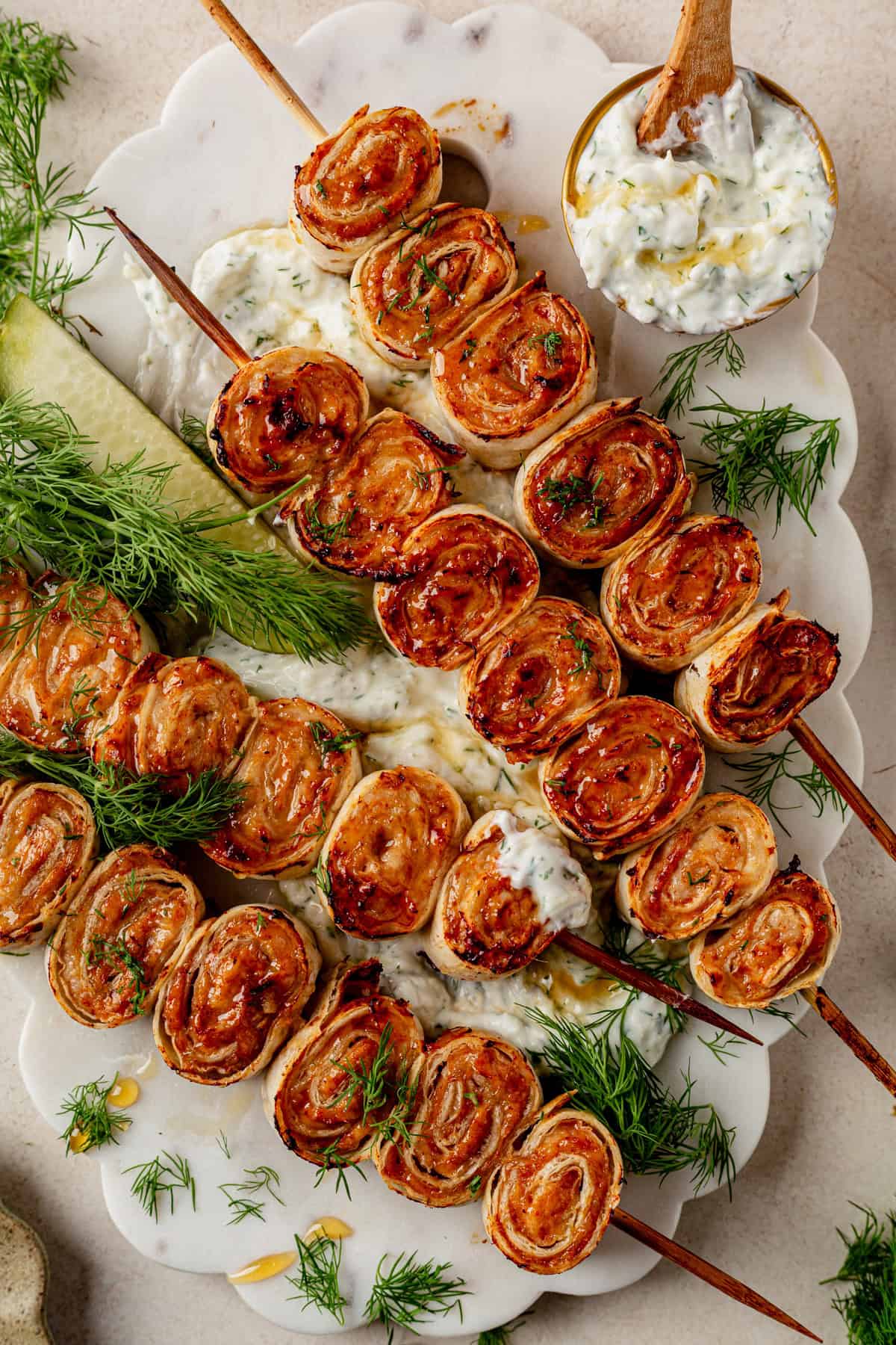 4 lazy kebab rolls on a platter with tzatziki sauce on the side.