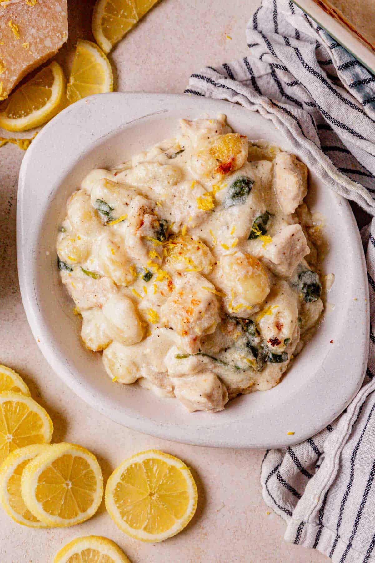 a bowl of creamy lemon chicken gnocchi with lemon slices next to it.
