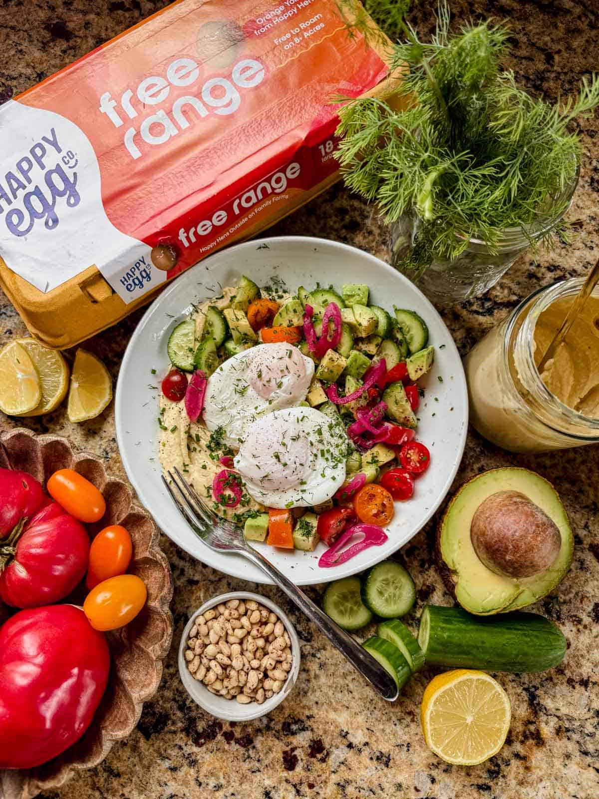 a mediterranean breakfast bowl next to a carton of happy egg free range eggs.