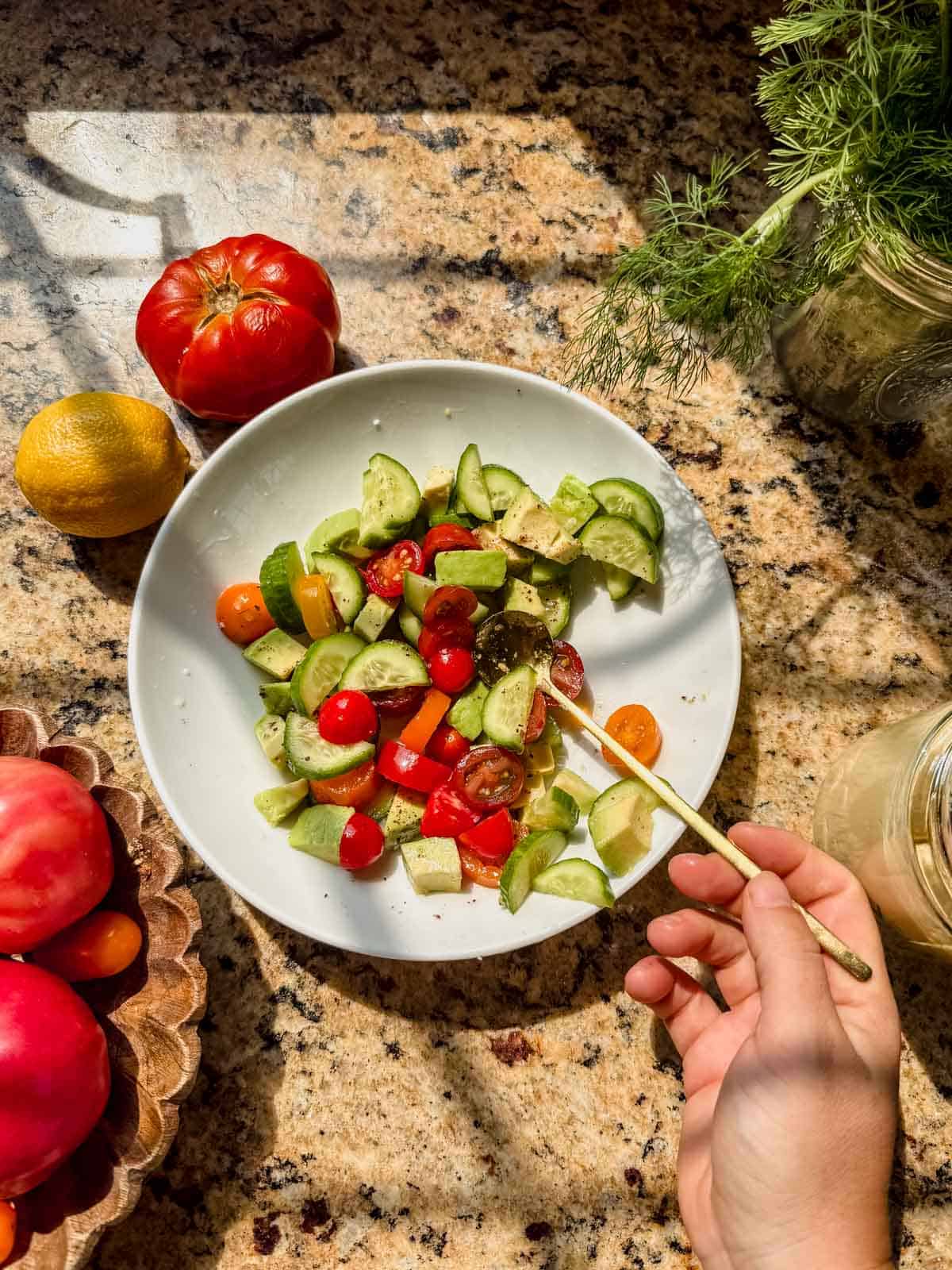 tossing cucumber, tomato, and avocado together for a mediterranean salad.