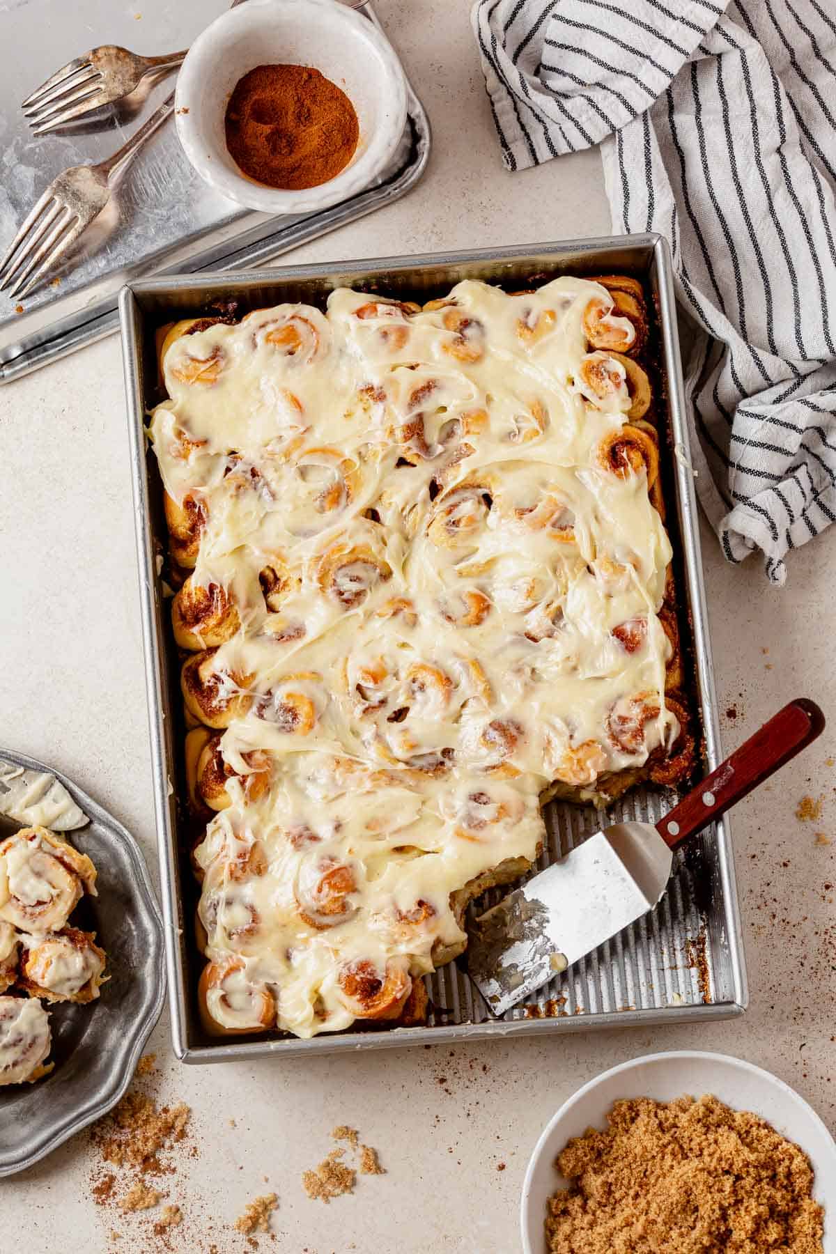 a pan of frosted mini cinnamon rolls with several missing from the corner and on a plate next to the pan.