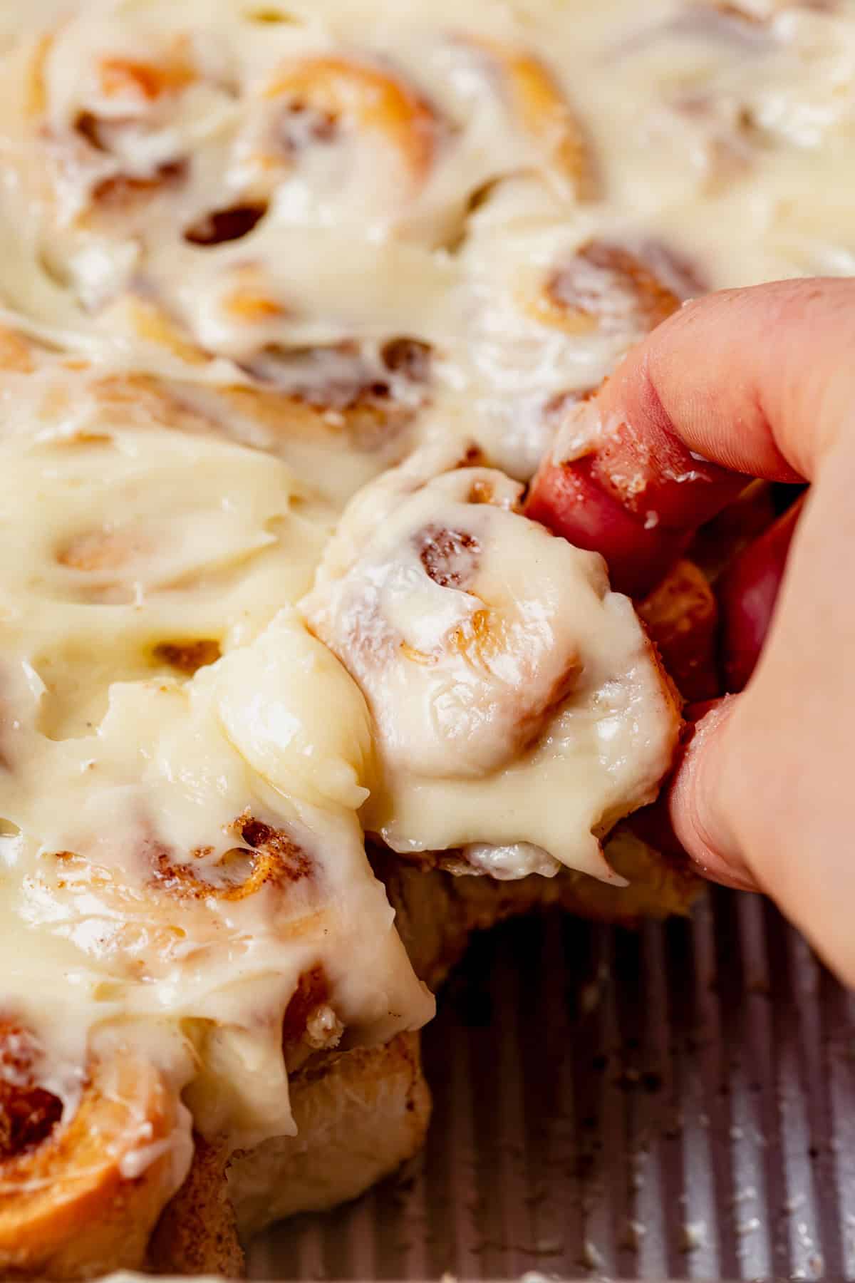 pulling a mini cinnamon roll apart from the other rolls.