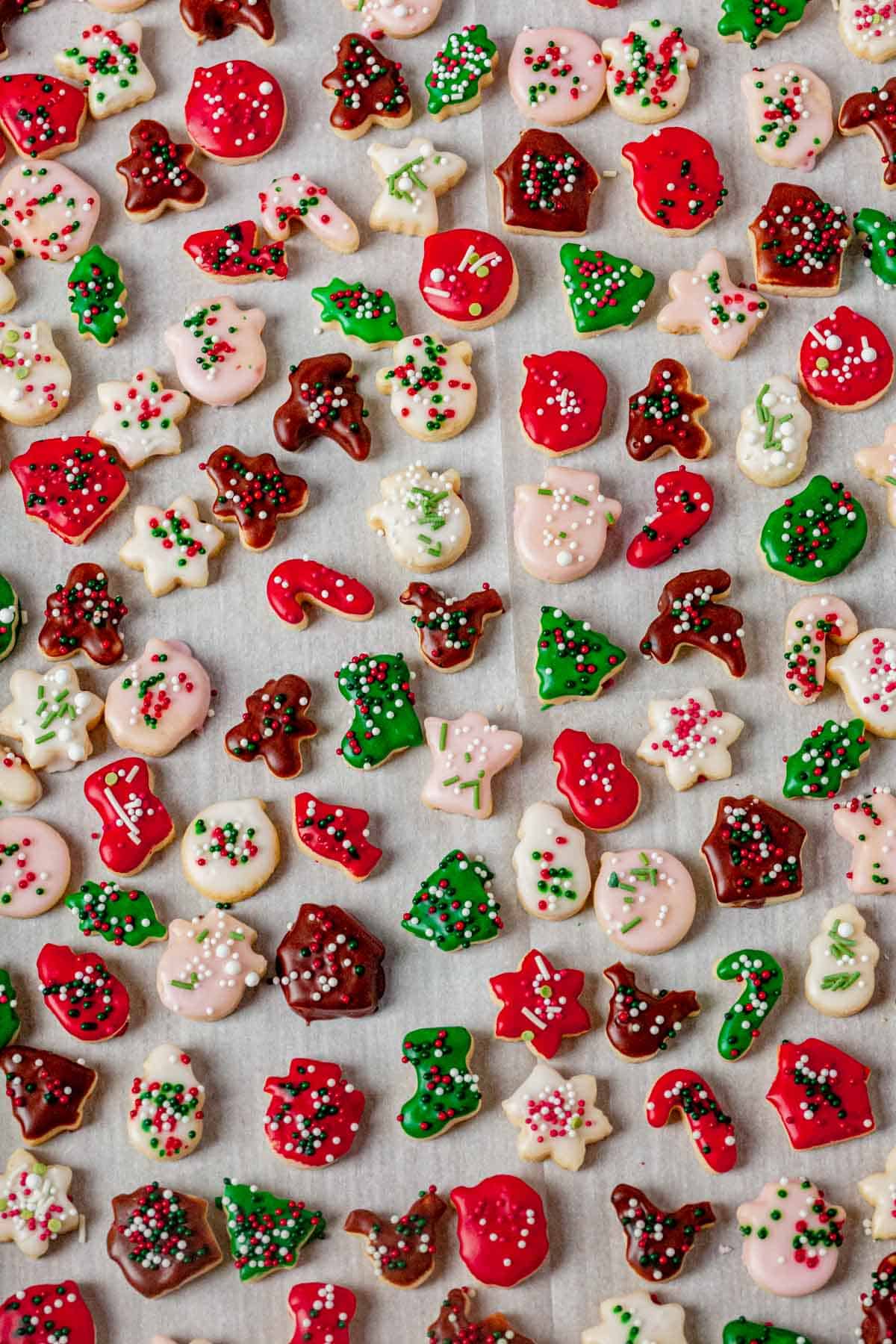 mini christmas sugar cookies with icing and sprinkles setting on a baking sheet.
