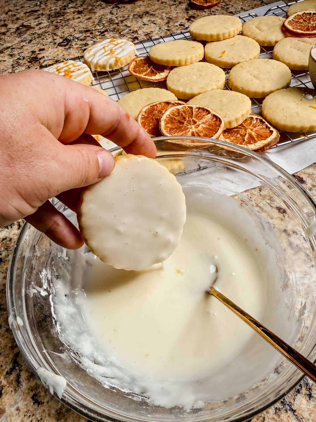 dipping an orange shortbread cookie into a bowl of orange glaze.