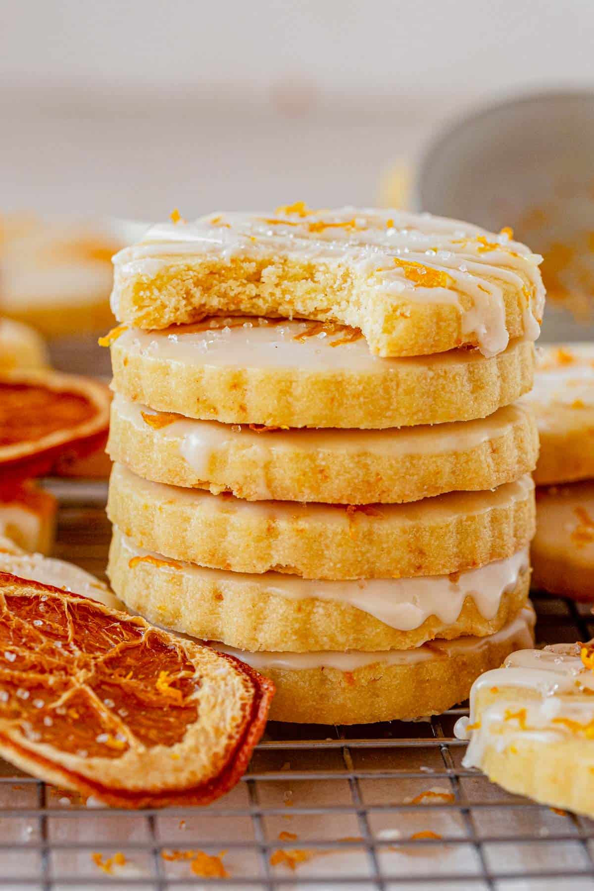 a stack of glazed orange shortbread cookies on a cooling rack.