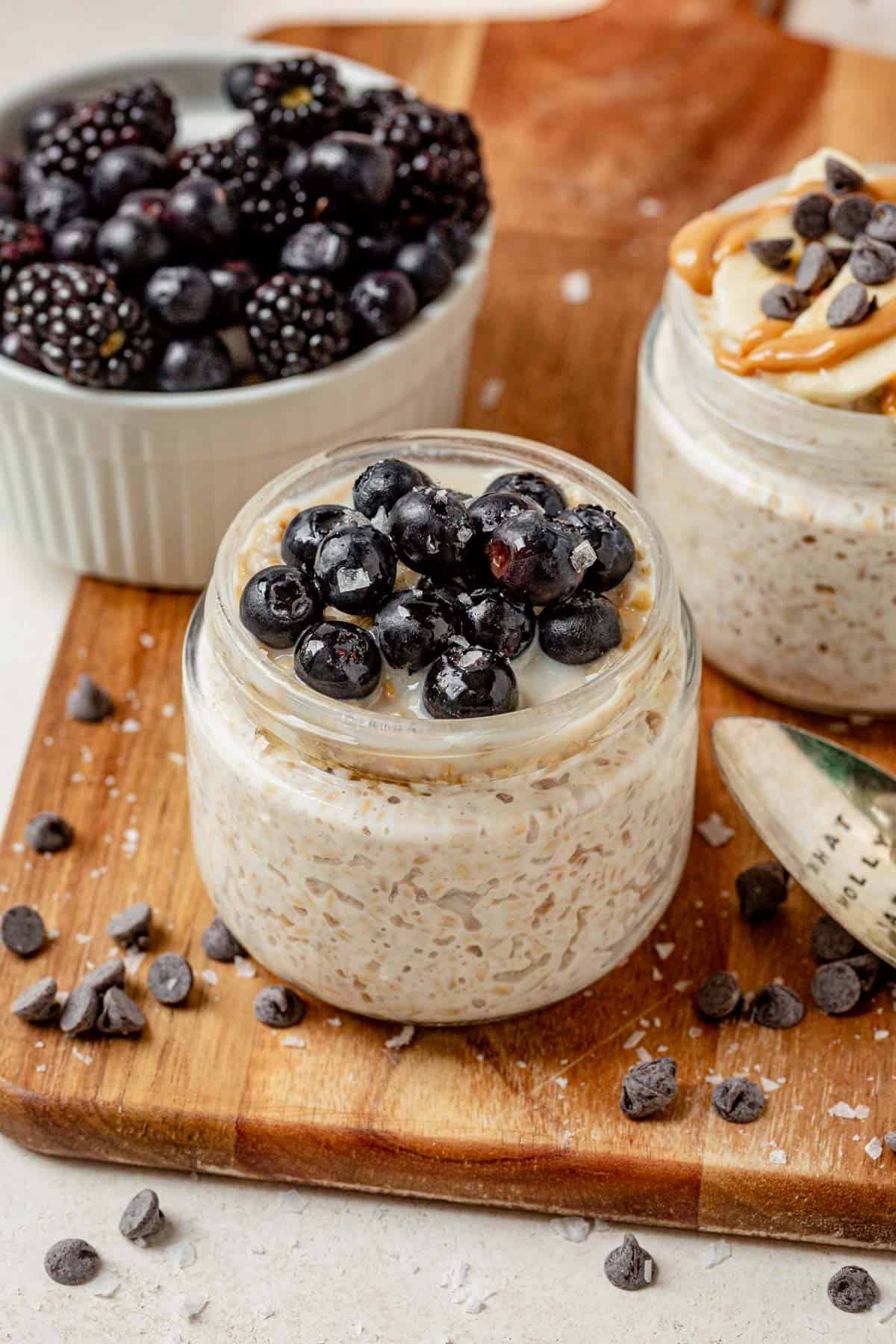Two jars of overnight steel cut oats on a serving board with fresh blueberries and honey.