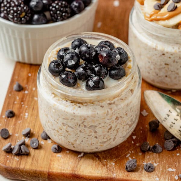 Creamy overnight steel cut oats in a glass jar topped with blueberries and a drizzle of honey.