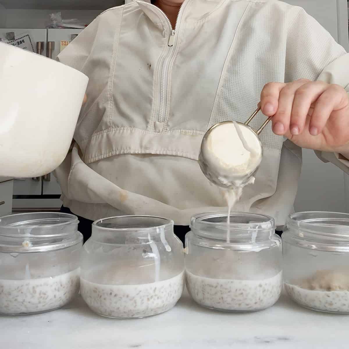 dividing overnight steel cut oats into glass meal prep jars.