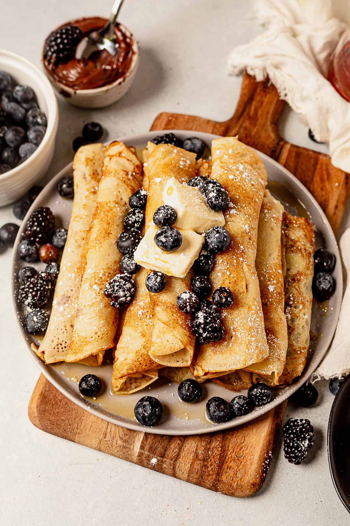 a plate of pancake roll ups with fresh berries, powdered sugar, and syrup