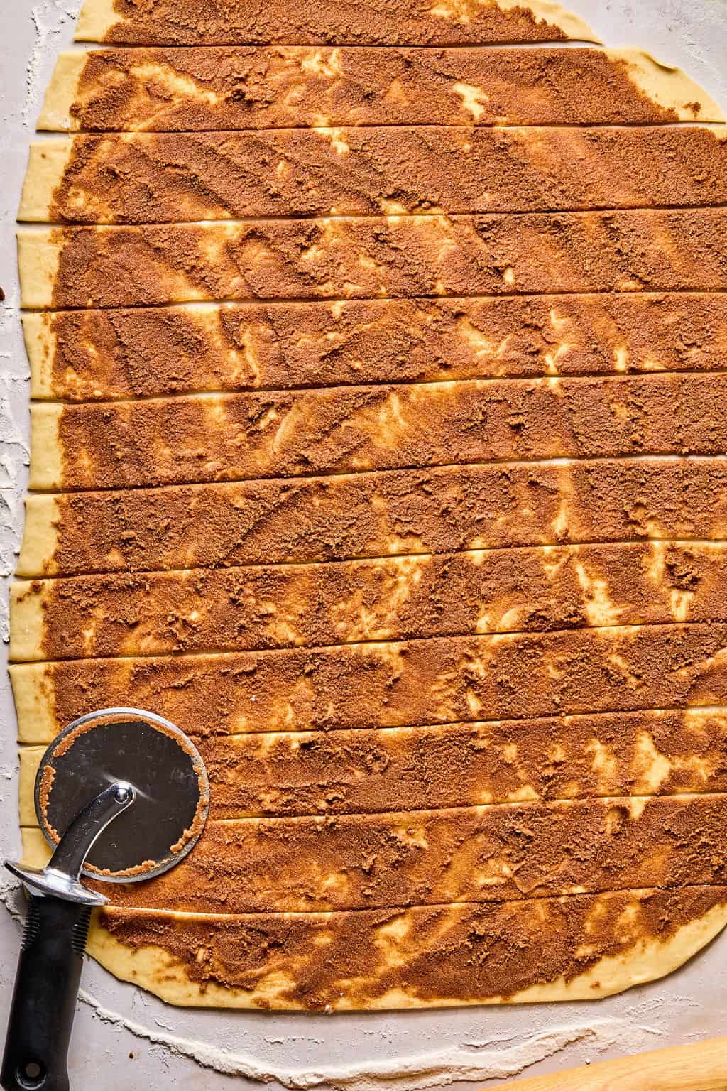 cinnamon roll dough rolled into a large rectangle and coated with cinnamon filling then cut into strips.