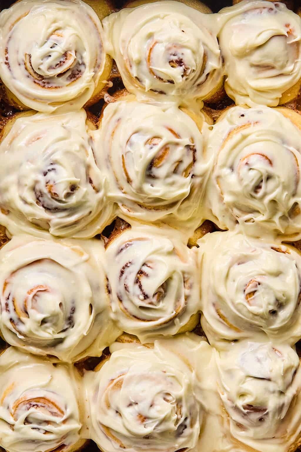 close up photo of gooey soft cinnamon rolls coated in cream cheese frosting.