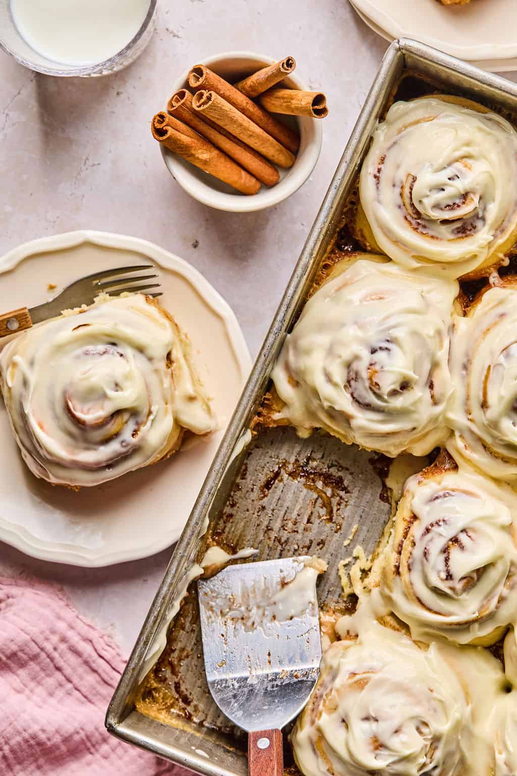 a pan of big gooey and soft cinnamon rolls with one on a plate next to the pan.