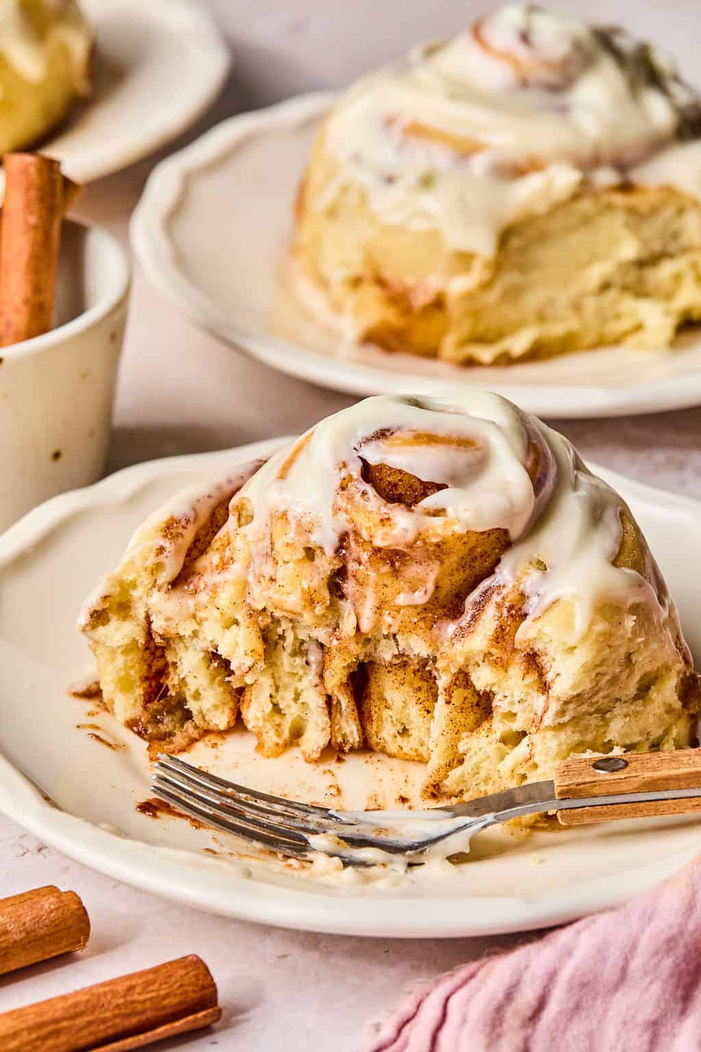 a cinnamon roll on a plate with a piece missing to see the soft and gooey center.