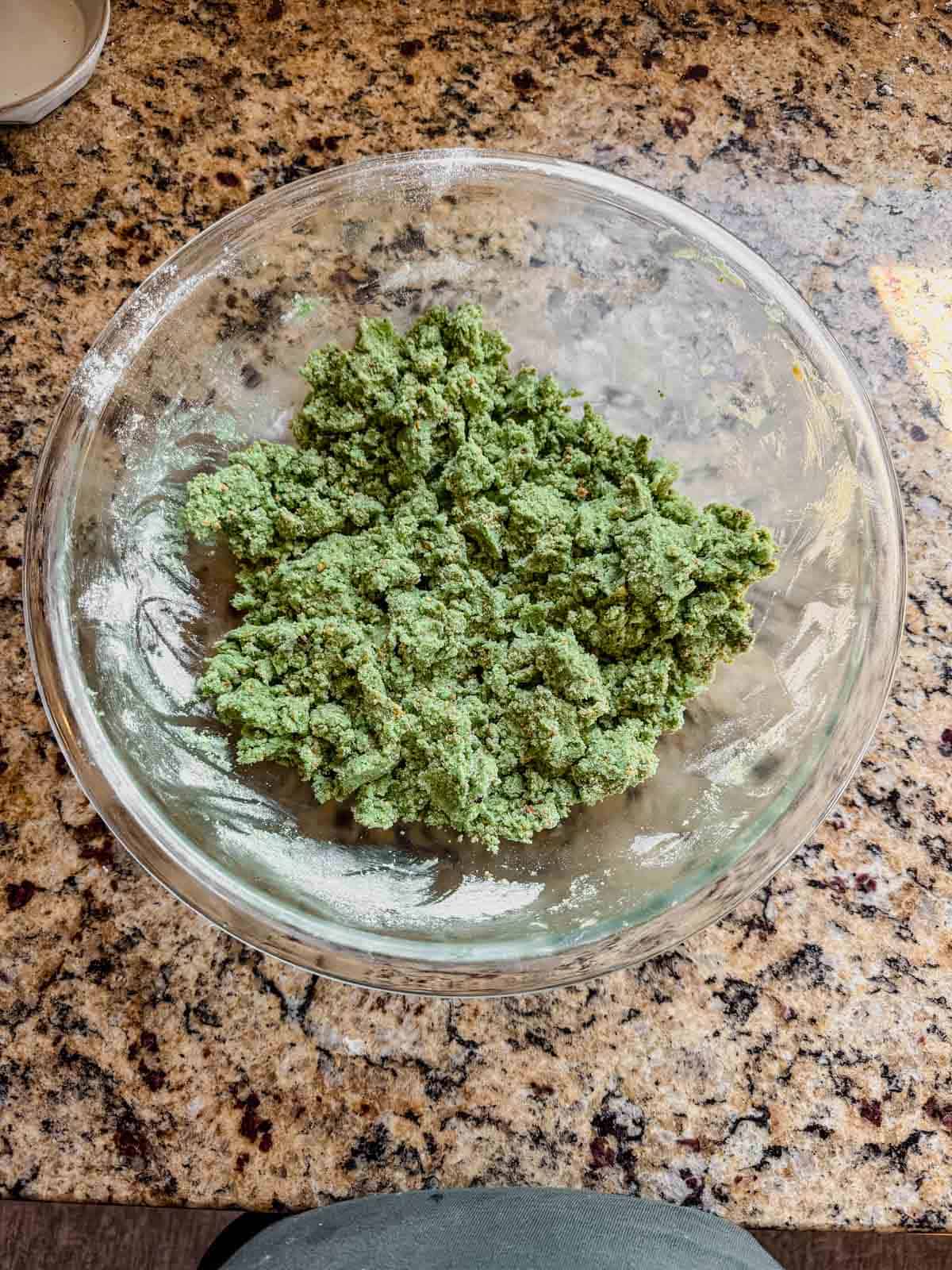 wet and dry ingredients for pistachio linzer cookie dough mixed together in a glass bowl on a counter