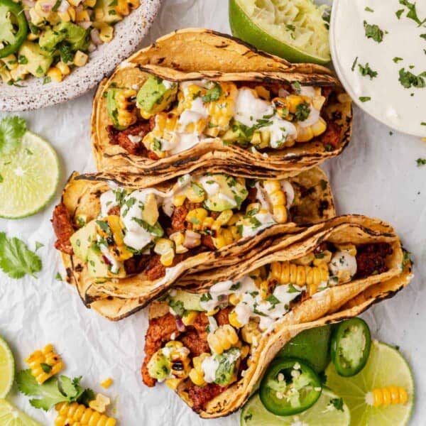 three pork tenderloin tacos topped with avocado corn salsa and crema