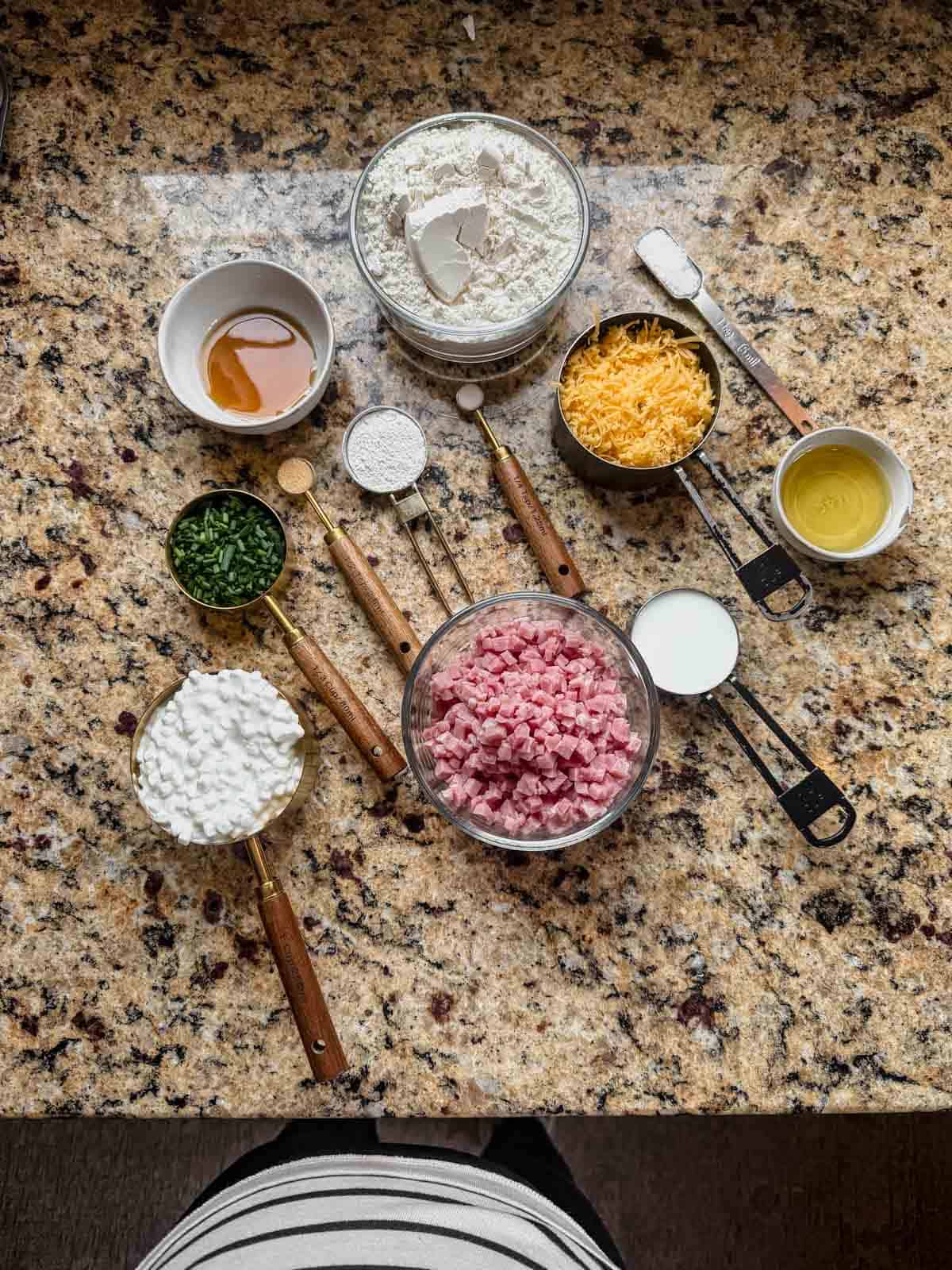 flour, baking powder, ham, cheese, cottage cheese, chives, and cheddar on a countertop.